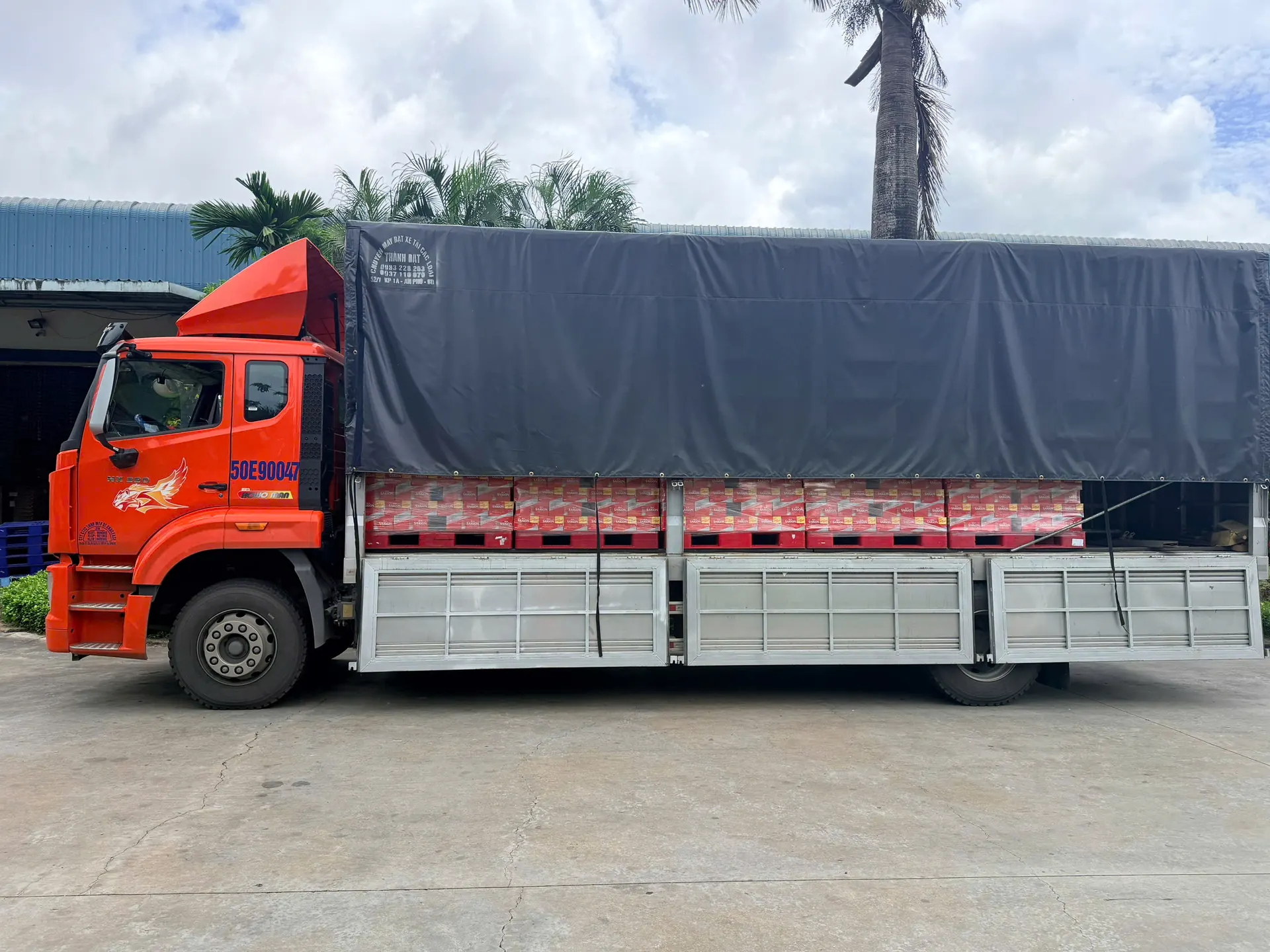 Xe tải màu cam của MEKONG TRANSPORT chở các pallet bia Sài Gòn, đậu trước kho hàng